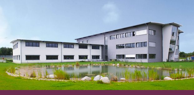 Modernes Gebäude vor einem Teich mit grüner Wiese